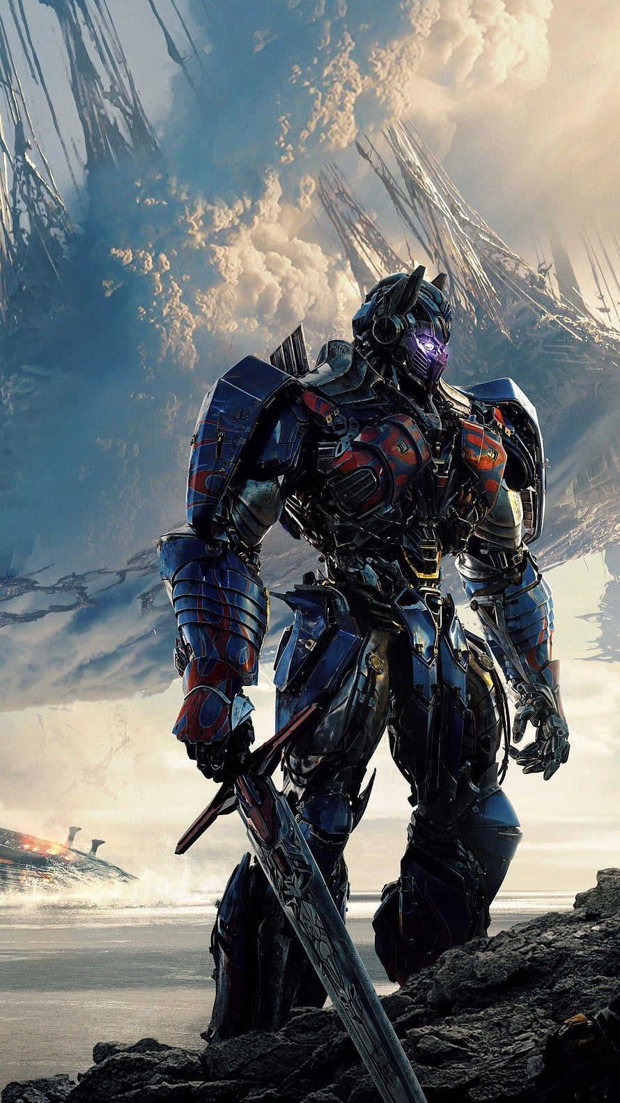 Optimus Prime wielding a sword in a dramatic sci-fi landscape with futuristic ruins and clouds HD phone wallpaper