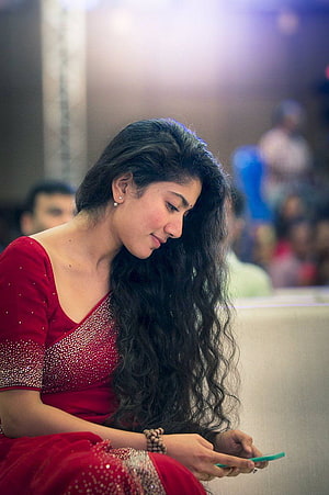 Sai Pallavi in a red embellished saree looking at a smartphone at a public event HD phone wallpaper