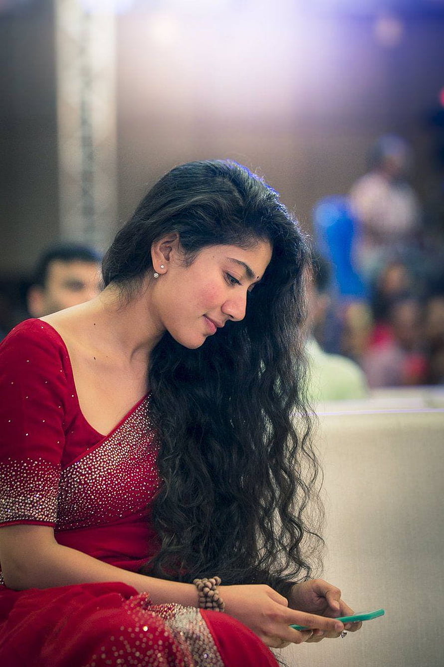 Sai Pallavi in a red embellished saree looking at a smartphone at a public event HD phone wallpaper