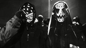 Black and white photo of two masked figures in hooded jackets at a nighttime event HD wallpaper