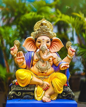 Colorful Ganesha Statue with Golden Crown and Yellow Dhoti Sitting on Blue Pedestal HD phone wallpaper