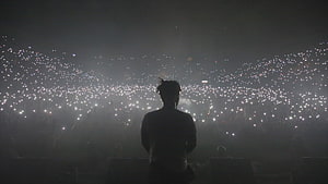 Silhouette of a performer on stage facing a massive crowd holding up thousands of glowing lights HD wallpaper