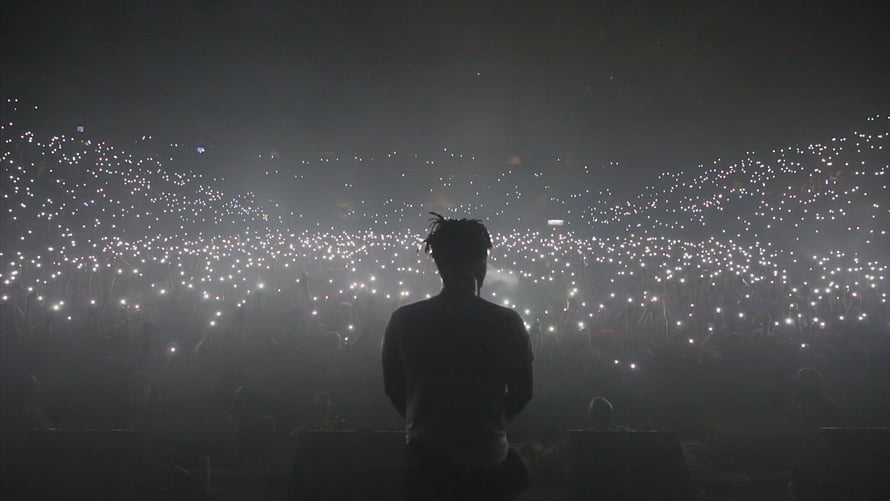 Silhouette of a performer on stage facing a massive crowd holding up thousands of glowing lights HD wallpaper