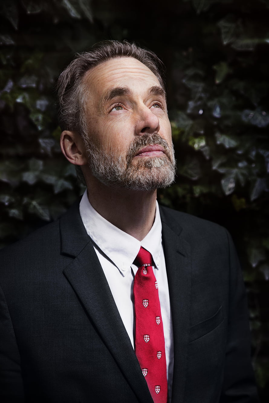 Jordan Peterson in a black suit and red tie against a dark ivy background HD phone wallpaper