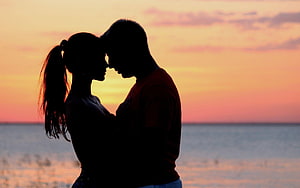 Silhouetted couple embracing at sunset by the ocean HD wallpaper