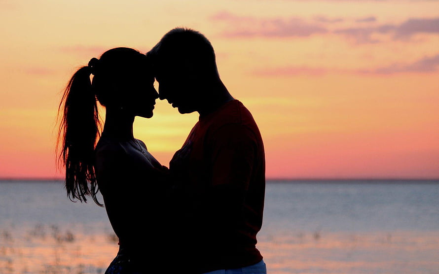 Silhouetted couple embracing at sunset by the ocean HD wallpaper