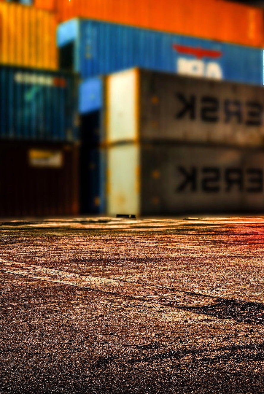 Low Angle View of Textured Asphalt with Blurred Shipping Containers in Background HD phone wallpaper