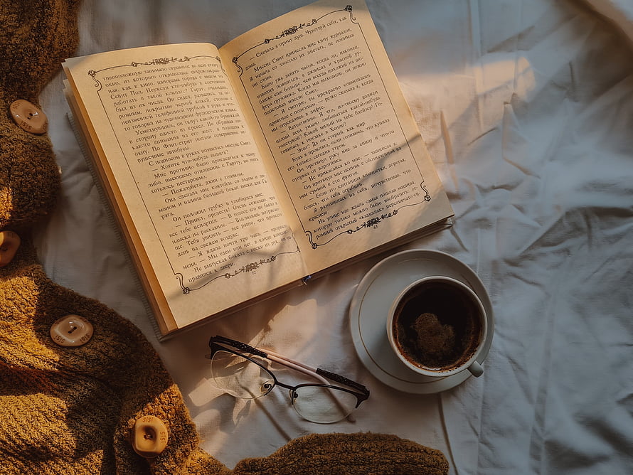 Cozy Reading Setup With Open Book, Coffee Cup, Glasses, And Knitted Sweater On Bed HD wallpaper