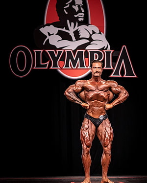 Bodybuilder posing on stage at the Olympia competition with extreme muscle definition HD phone wallpaper