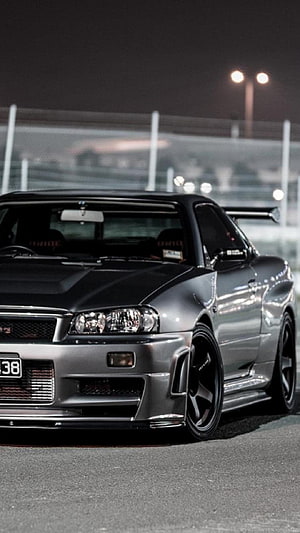 Silver Nissan Skyline GT-R R34 on a racetrack at night with street lights HD phone wallpaper