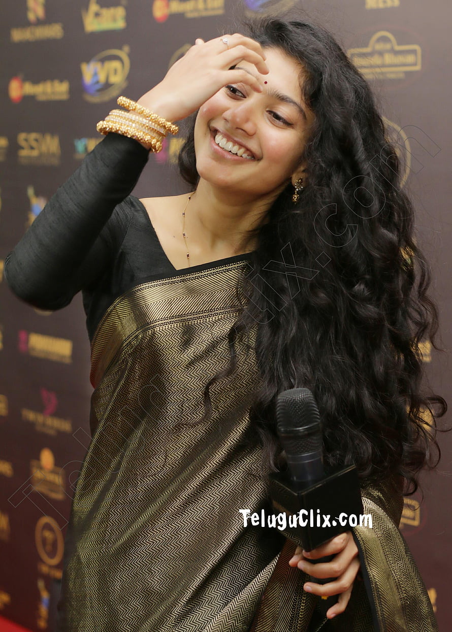 Sai Pallavi smiling at a media event in a gold and black saree holding a microphone HD phone wallpaper