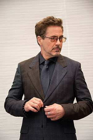 Robert Downey Jr in a tailored dark suit and amber glasses against a neutral studio backdrop HD phone wallpaper