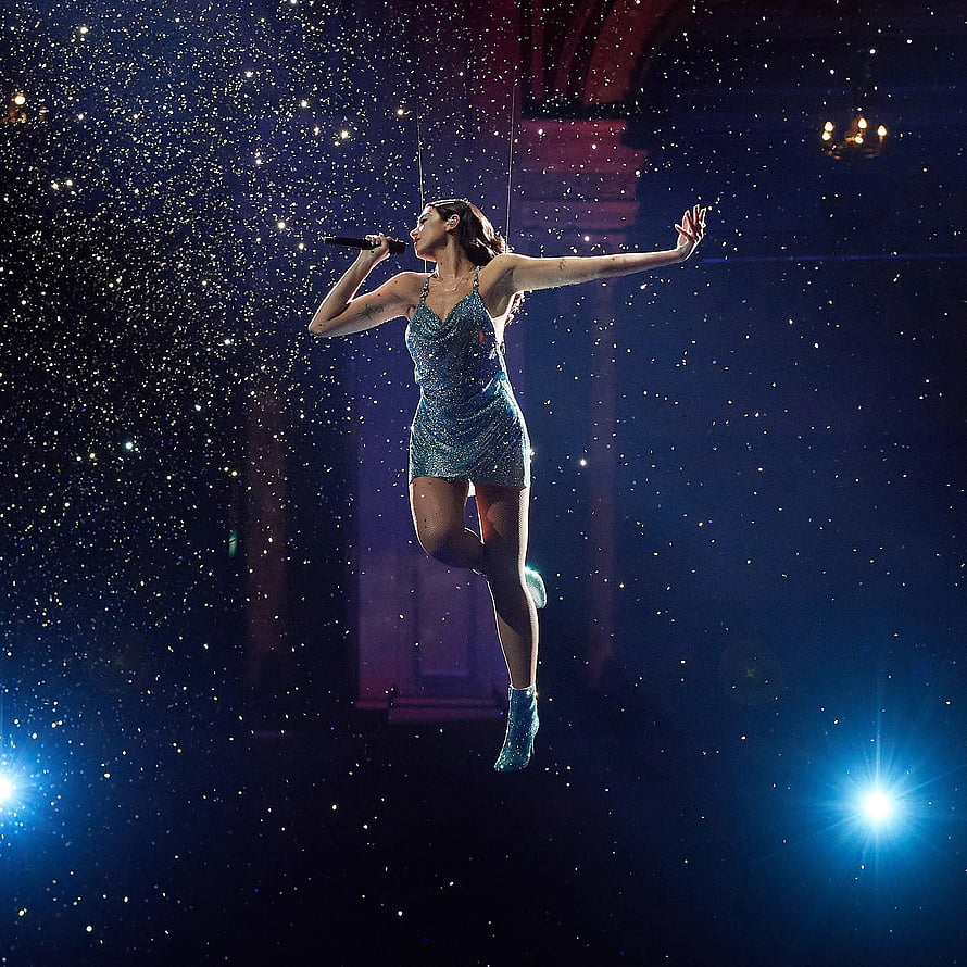 Dua Lipa performing in a sparkling blue dress suspended mid-air on stage with glittering confetti and dramatic lighting HD phone wallpaper