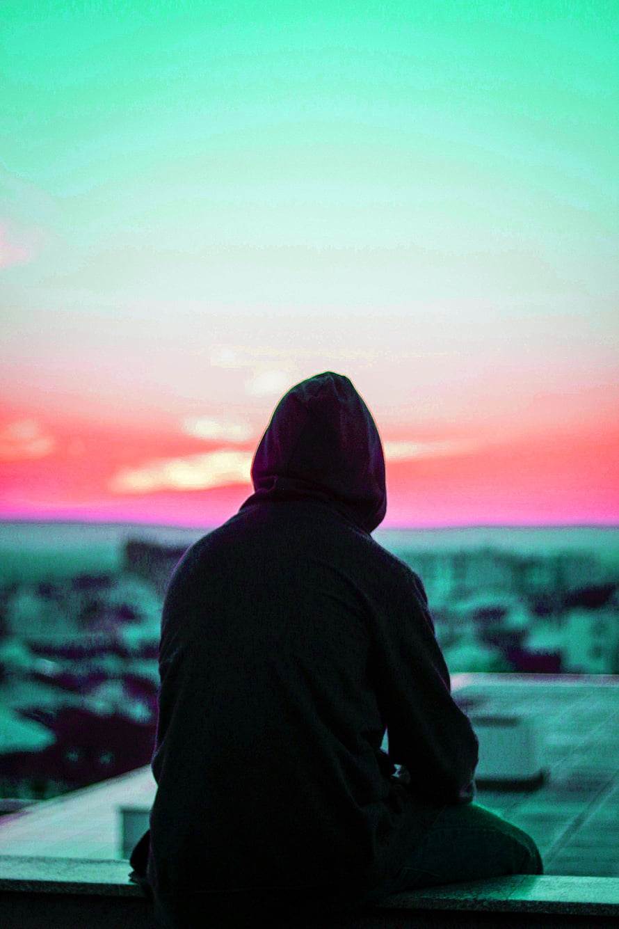 Silhouette of a Hooded Figure Sitting on a Rooftop at Sunset HD phone wallpaper