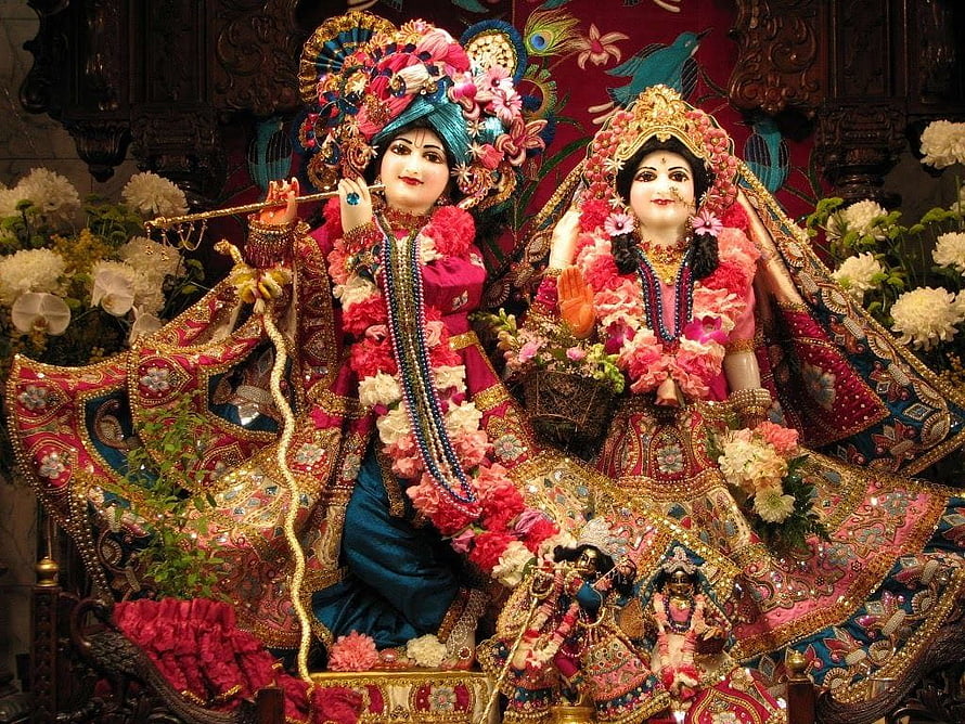 Radha Krishna idols adorned in vibrant floral garlands and intricate traditional attire HD wallpaper