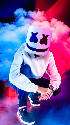 Marshmello DJ in white hoodie crouching with neon blue and pink smoke backdrop HD phone wallpaper