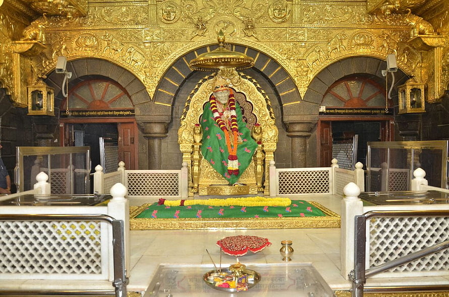 Sai Baba shrine with golden canopy, green dhoti, and marigold garlands in ornate temple sanctum HD wallpaper