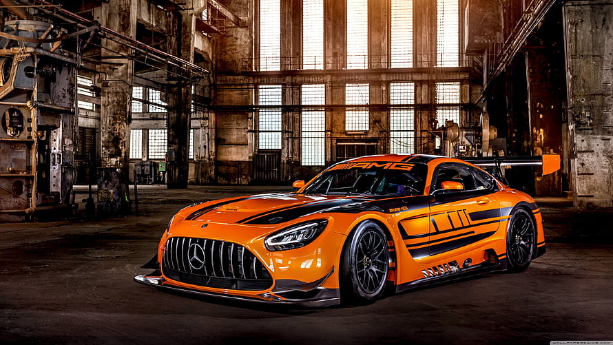 Orange Mercedes-AMG GT3 race car parked inside a dim industrial warehouse with dramatic lighting HD wallpaper