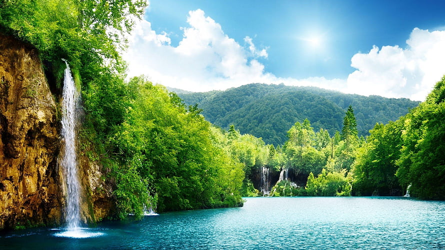 Serene Waterfall Cascading Into Turquoise Lake Surrounded by Lush Green Forest HD wallpaper