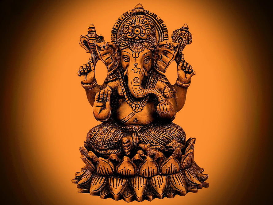Ganesha seated on lotus with four arms and ornate headdress in warm golden tones HD wallpaper