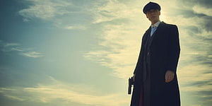 Tommy Shelby from Peaky Blinders in a long coat and flat cap holding a pistol against a dramatic sky HD wallpaper
