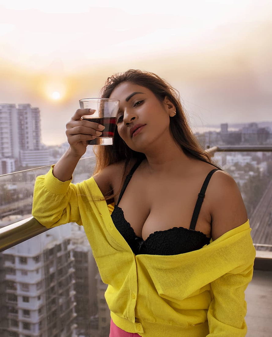 Muskan Agarwal on a rooftop terrace at sunset holding a glass of red wine in a yellow cardigan HD phone wallpaper