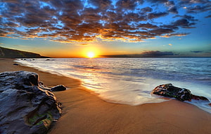 Golden sunset over a rocky shoreline with dramatic clouds and calm ocean waves HD wallpaper