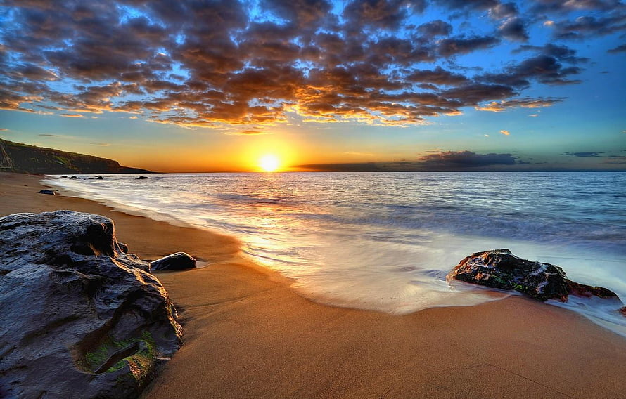 Golden sunset over a rocky shoreline with dramatic clouds and calm ocean waves HD wallpaper