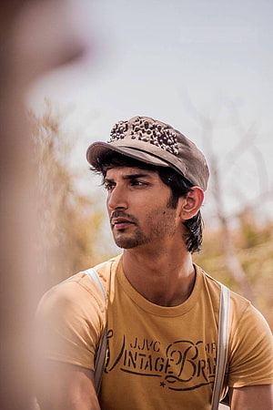 Sushant Singh Rajput in a mustard t-shirt and studded cap with a contemplative expression HD phone wallpaper