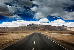 Endless Highway Stretching Through Arid Mountain Landscape Under Dramatic Clouds HD wallpaper