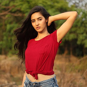 Simrat Kaur in a red tied t-shirt and denim shorts posing outdoors with long dark hair HD phone wallpaper