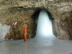 Mysterious Orange Figure Standing in a Glowing Ice Cave with Frozen Waterfall HD wallpaper