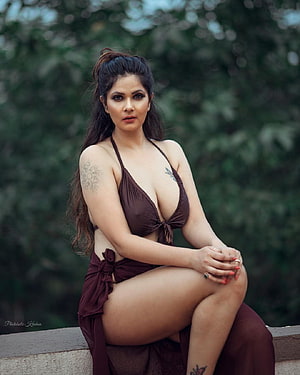 Aabha Paul in a Maroon Bikini Sitting on a Stone Wall with Lush Green Foliage in the Background HD phone wallpaper
