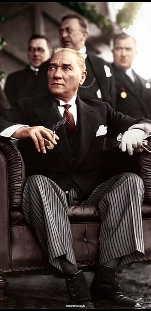 Mustafa Kemal Ataturk sitting in a leather chair smoking a cigarette with associates in the background HD phone wallpaper
