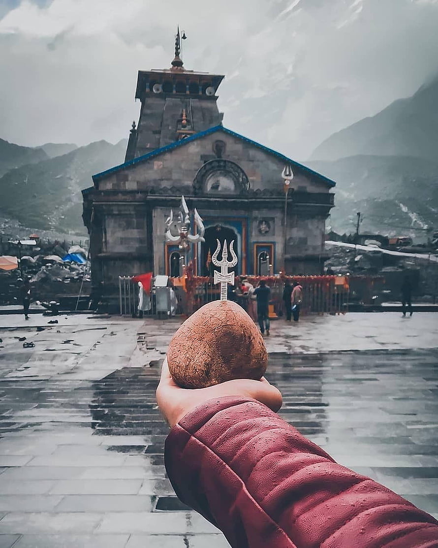 Hand holding a coconut with a trident in front of Kedarnath Temple in the Himalayas HD phone wallpaper