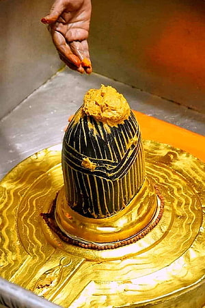 Close-up of a Shiva Lingam being anointed with turmeric paste in a Hindu temple ritual HD phone wallpaper