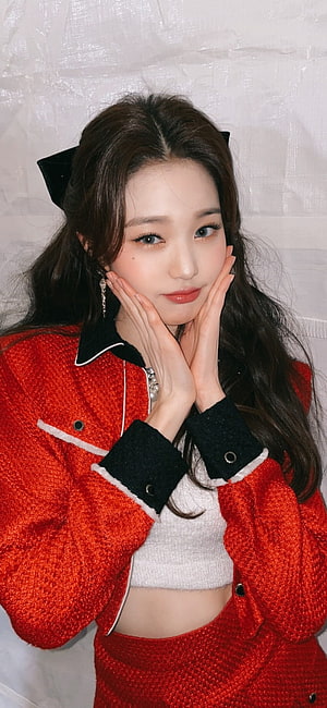 Wonyoung in a red tweed jacket with black collar and cuffs, hands framing her face HD phone wallpaper
