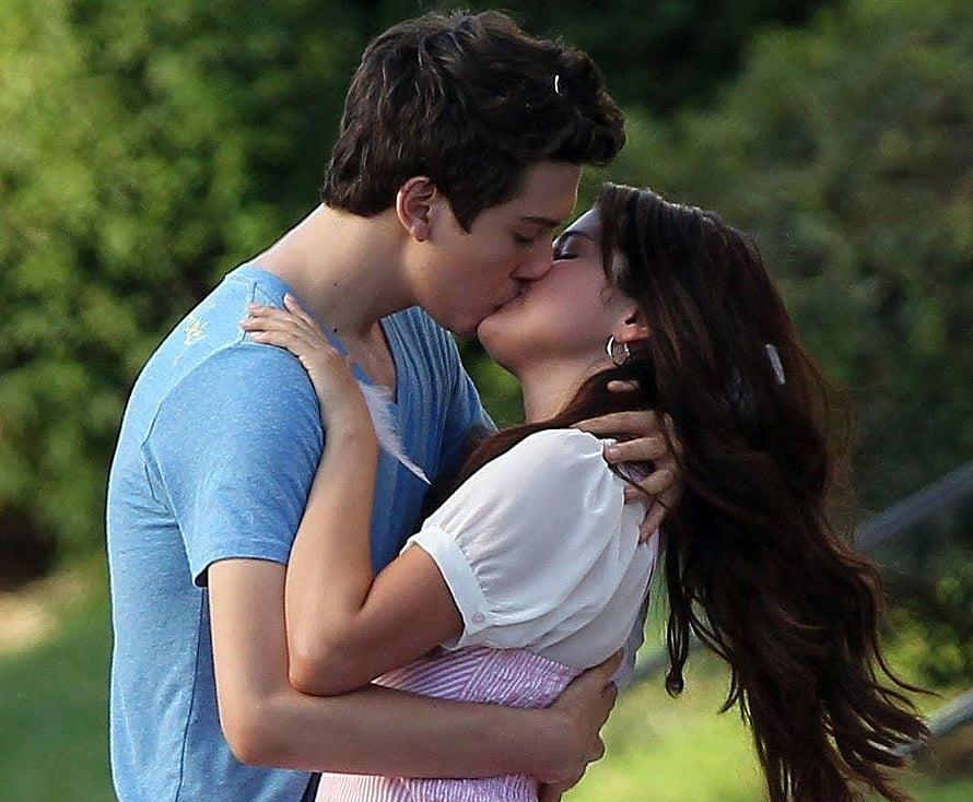 Young couple sharing a passionate kiss in a sunlit outdoor garden setting HD wallpaper