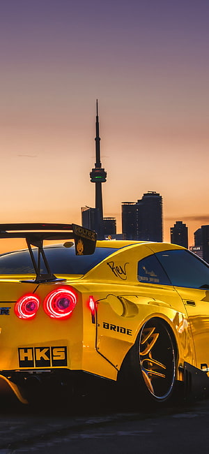 Yellow Nissan GT-R with HKS and Bride Stickers Parked Against Toronto Skyline at Sunset HD phone wallpaper