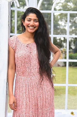 Sai Pallavi in a pink floral dress standing by a white window frame HD phone wallpaper