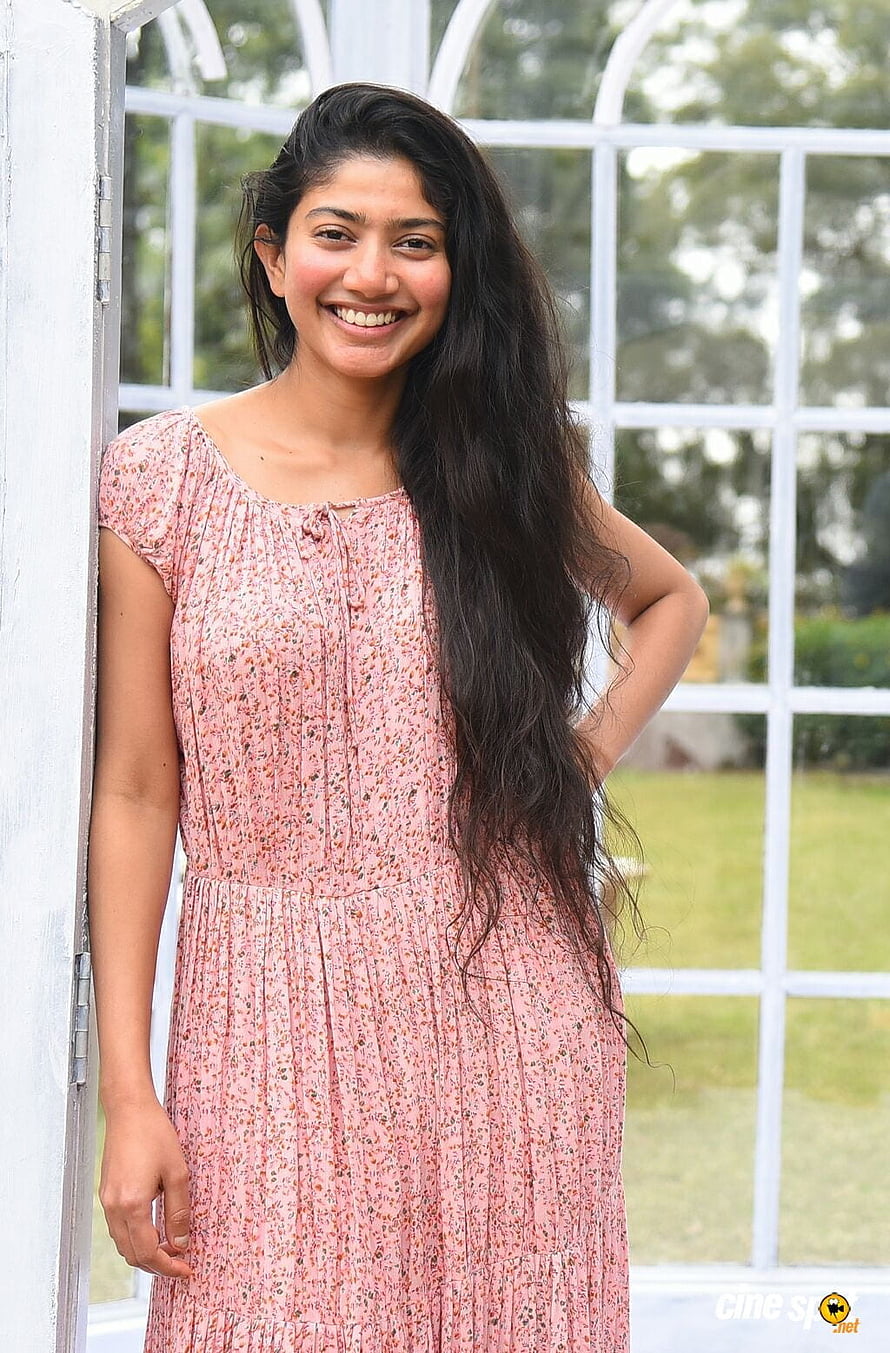 Sai Pallavi in a pink floral dress standing by a white window frame HD phone wallpaper