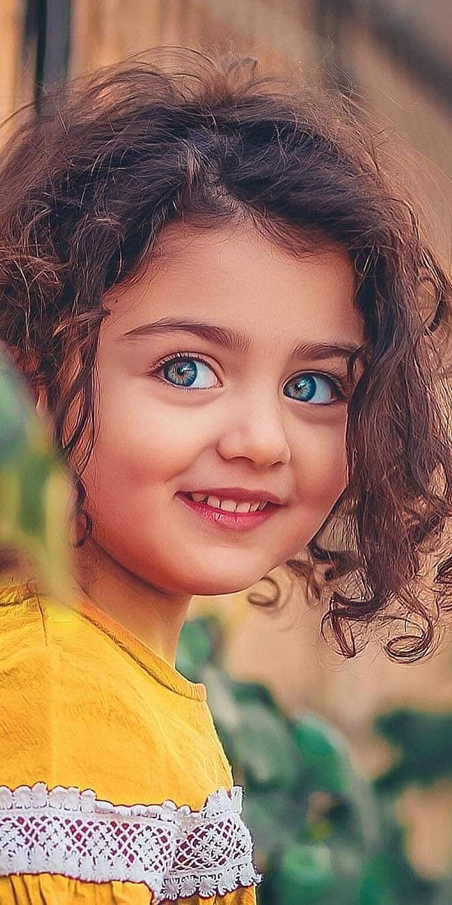 Portrait of a cute little girl with curly brown hair and bright blue eyes smiling in a yellow dress HD phone wallpaper