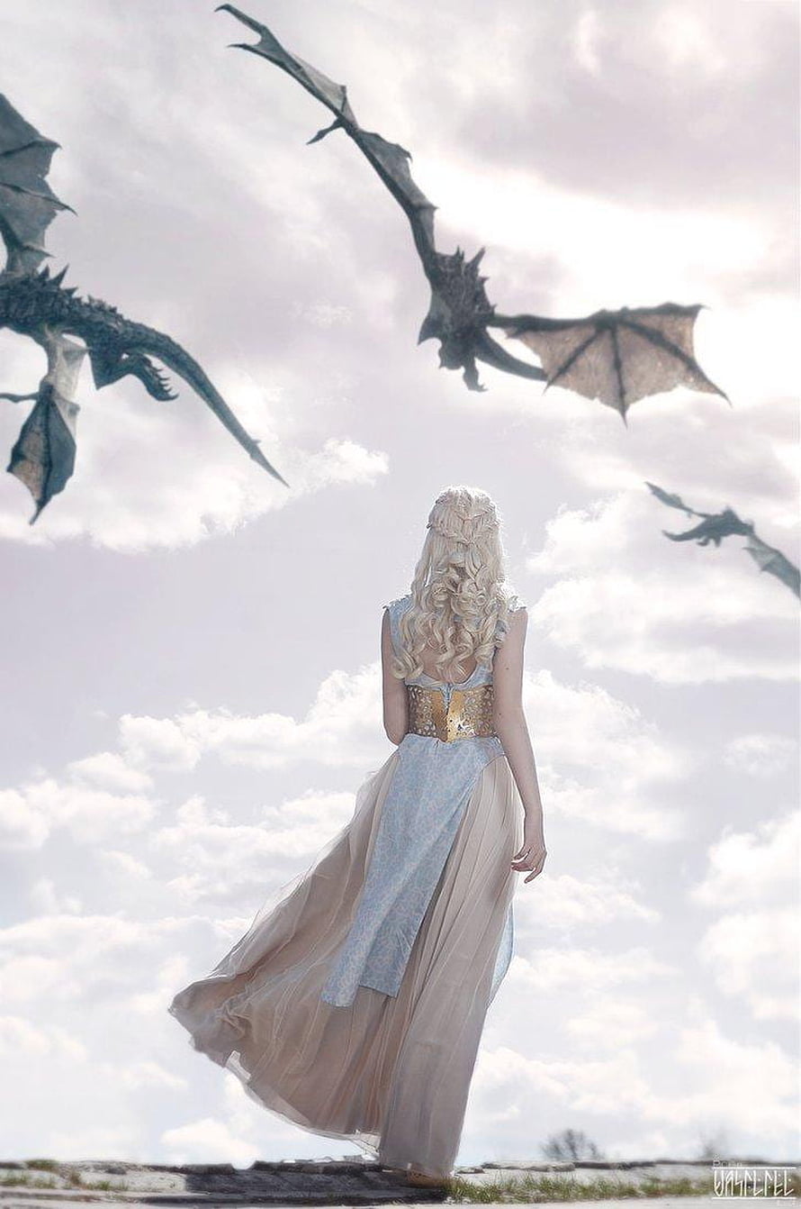 Daenerys Targaryen in flowing gown gazing at dragons soaring through a cloudy sky HD phone wallpaper