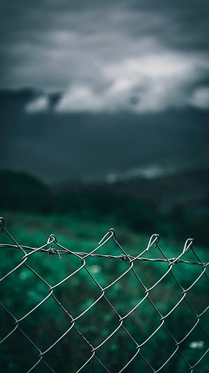 Moody Chain Link Fence Against Stormy Mountains and Green Fields HD phone wallpaper