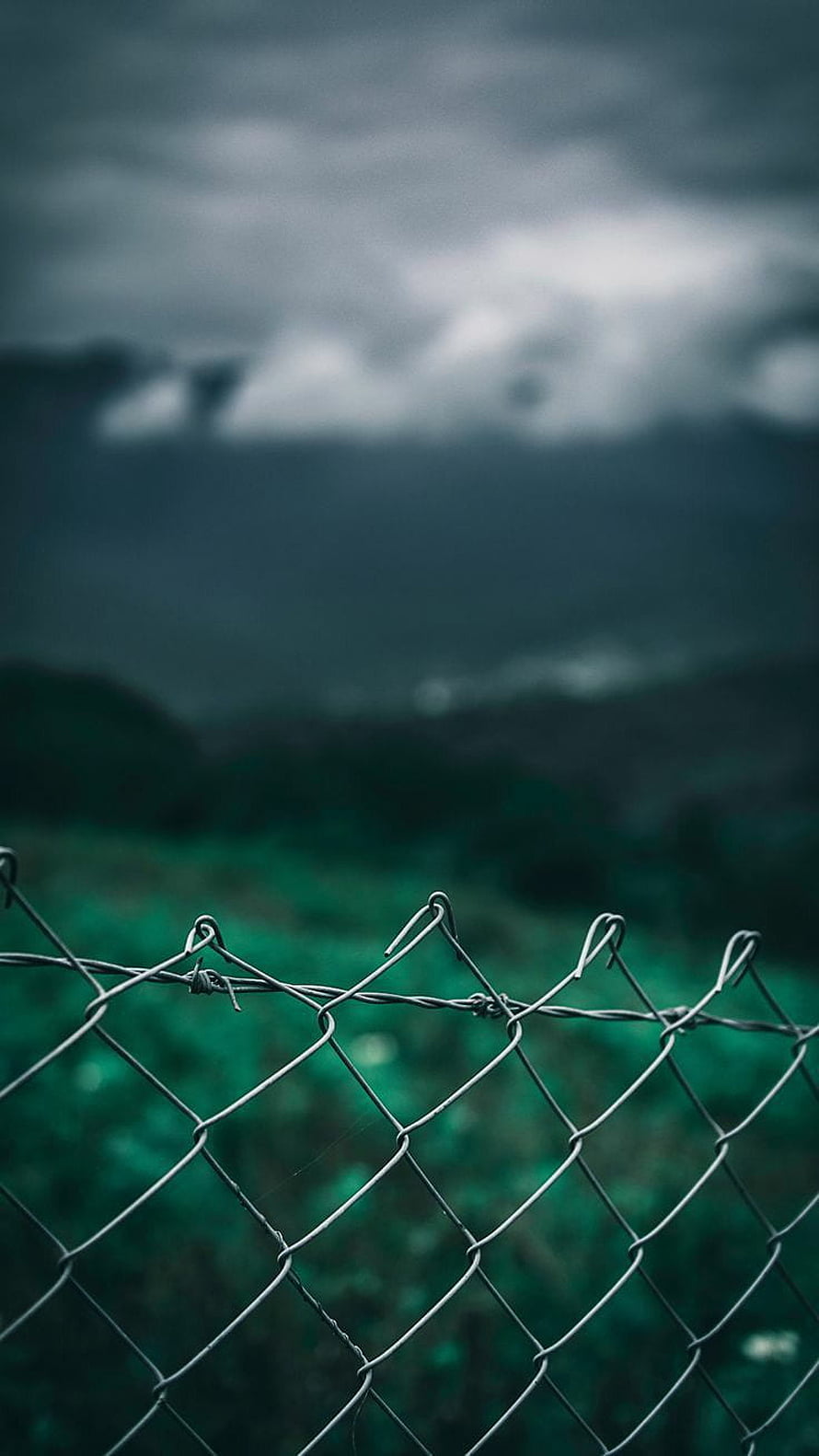 Moody Chain Link Fence Against Stormy Mountains and Green Fields HD phone wallpaper