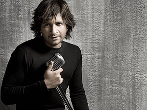 A man in a black sweater holding a vintage microphone against a textured gray wall, Best 5 Kk on Hip, kk singer HD wallpaper