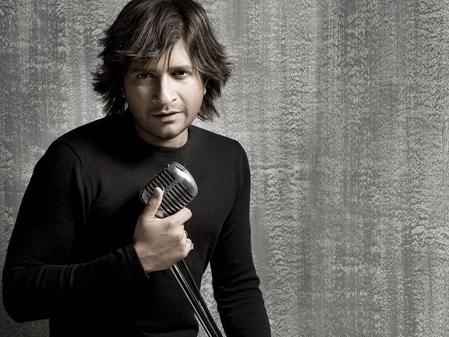 A man in a black sweater holding a vintage microphone against a textured gray wall, Best 5 Kk on Hip, kk singer HD wallpaper