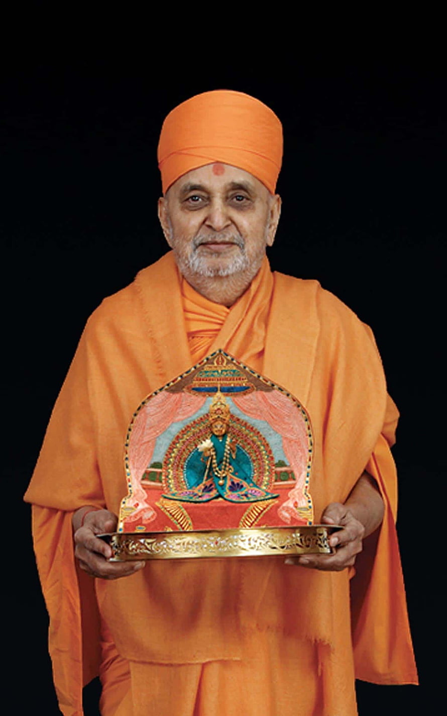 HH Pramukh Swami Maharaj in saffron robes holding a traditional deity portrait on a golden tray HD phone wallpaper