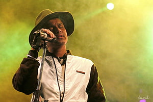 Zubeen Garg performing live on stage with a microphone and wide-brimmed hat under green concert lighting HD wallpaper