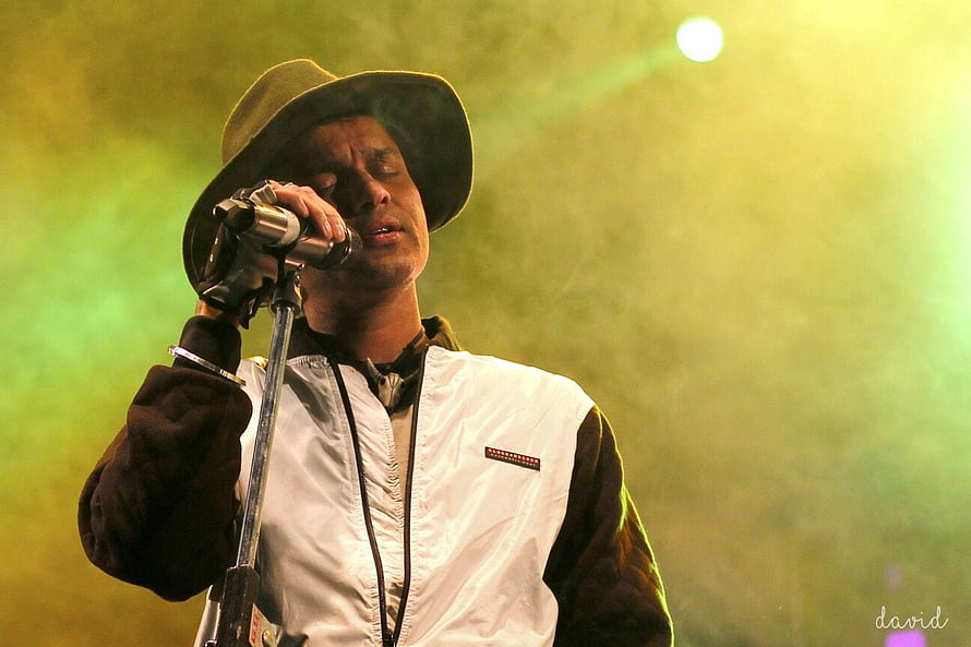 Zubeen Garg performing live on stage with a microphone and wide-brimmed hat under green concert lighting HD wallpaper